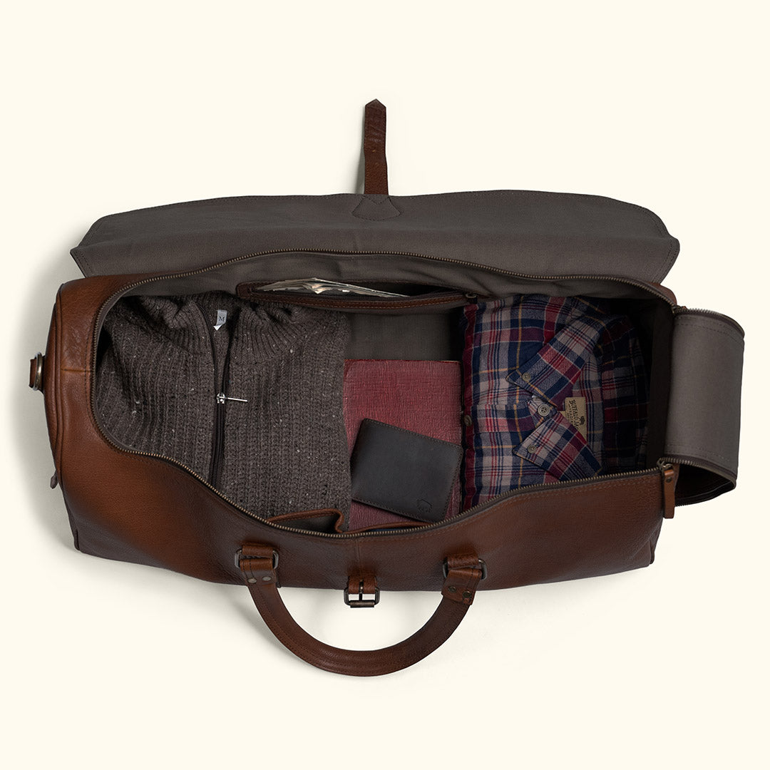 What fits in a Roosevelt leather duffle bag — clothes, shoes, dopp kit, and gear laid out around the open bag