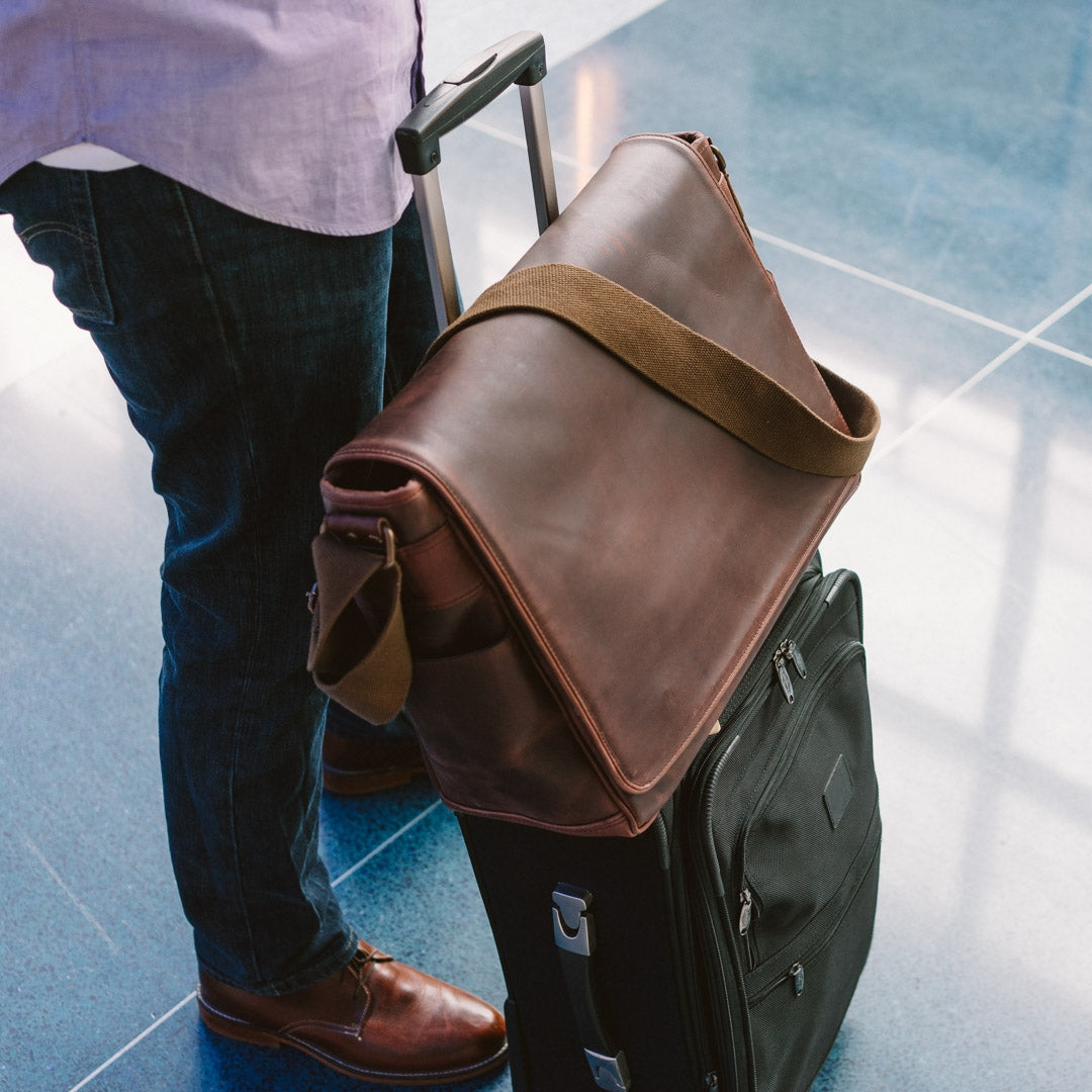 Large dark oak leather satchel with wide strap, perfect for secure attachment to luggage during travel.